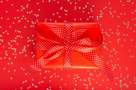 Festive background , gift box with ribbon and bow on a red background with glitter silver stars, flat lay, top viewの写真素材