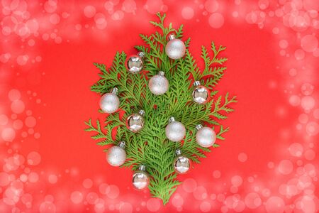 Decorative fir tree made of thuja twigs with silver Christmas balls on a red background, holiday backgroundの写真素材