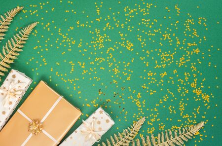 Festive background with decorations , bright shiny golden fern leaves and gift boxes on a green background with glitter gold stars, flat lay, top view, copy spaceの写真素材