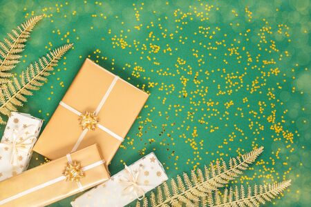 Festive background with decorations , bright shiny golden fern leaves and gift boxes on a green background with glitter gold stars, flat lay, top view, copy spaceの写真素材