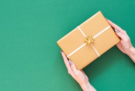 Festive background, girl holds gold gift box with bow on green background, merry christmas and happy new year concept, flat lay, top view, copy spaceの写真素材
