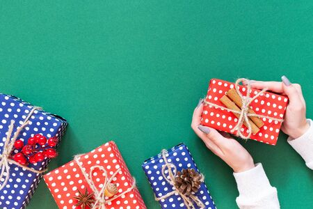 Girl holds gift box, red and blue gift boxes in polka dots with christmas tree cone and twigs of hawthorn with acorn and cinnamon on green background, flat lay, top viewの写真素材