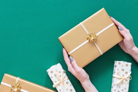 Festive background, girl holds gold gift box with bow, gift boxes on green background, merry christmas and happy new year concept, flat lay, top view, copy spaceの写真素材