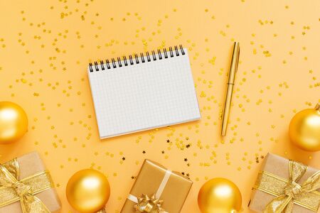 Holiday background, gold background with gift boxes and glitter gold christmas balls, open spiral notepad and pen, flat lay, top view, copy spaceの写真素材