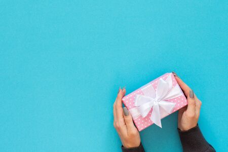 Girl holds gift box, pink gift box in polka dots with white ribbon and bow on a blue background , flat lay, top view, birthday or valentines dayの写真素材