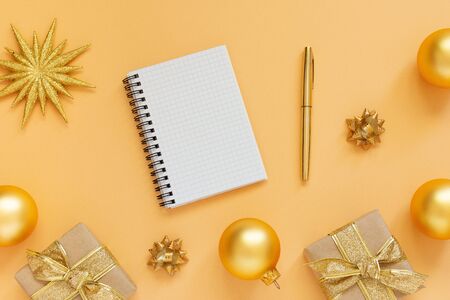 Holiday background, gold background with glitter gold star and gift boxes and christmas balls, open spiral notepad and pen, flat lay, top view, copy spaceの写真素材