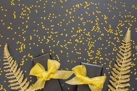 Festive background with gold decorations , shiny golden fern leaves and gift boxes on a black background with glitter gold stars , flat lay, top view, copy spaceの写真素材