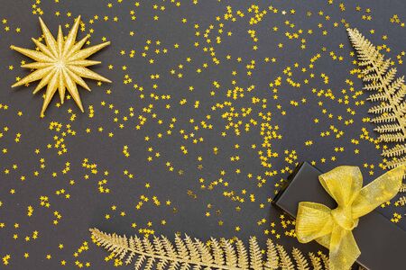 Festive background with gold decorations , shiny golden fern leaves and gift box on a black background with glitter gold stars , flat lay, top view, copy spaceの写真素材