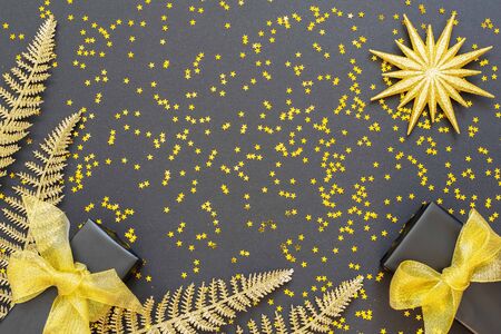 Festive background with gold decorations , shiny golden fern leaves and gift boxes on a black background with glitter gold stars , flat lay, top view, copy spaceの写真素材