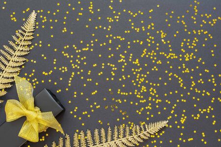 Festive background with gold decorations , shiny golden fern leaves and gift box on a black background with glitter gold stars , flat lay, top view, copy spaceの写真素材