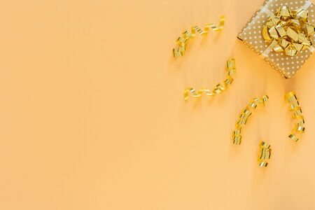 Holiday background in gold colors, gift box with shiny bow and with glitter ribbons serpentine on a gold background, flat lay, top view, copy spaceの写真素材