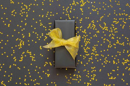 Festive background , gift box with shiny golden ribbon on a black background with glitter gold stars , flat lay, top viewの写真素材