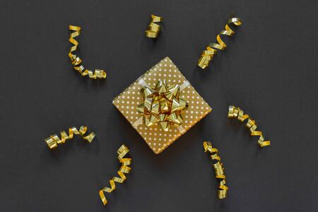 Holiday background in gold colors, gift box with shiny bow and with glitter ribbons serpentine on a black background, flat lay, top view, copy spaceの写真素材