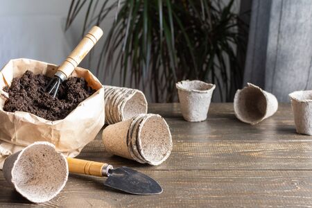 Eco friendly pots for seedlings on wooden background, small bag with ground and garden trowel and rakesの写真素材