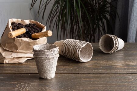 Eco friendly pots for seedlings on wooden background, small bag with ground and garden trowel and rakesの写真素材