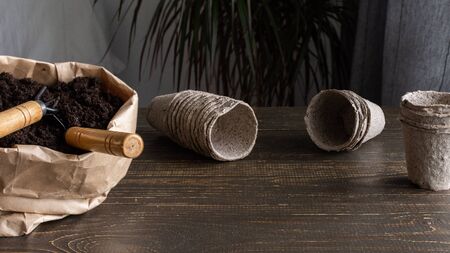 Eco friendly pots for seedlings on wooden background, small bag with ground and garden trowel and rakesの写真素材