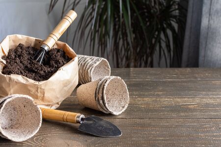 Eco friendly pots for seedlings on wooden background, small bag with ground and garden trowel and rakesの写真素材