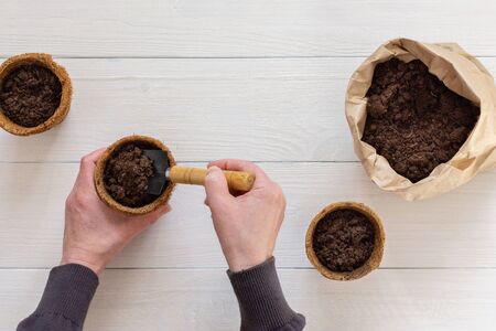 Eco friendly pots for seedlings and small bag with ground on a white wooden background, female hands with a garden shovel and ground , top viewの写真素材