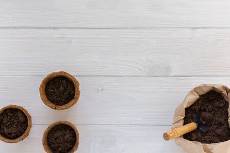 Eco friendly pots for seedlings on a white wooden background, small bag with ground and garden trowelの写真素材