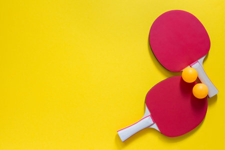 Red tennis rackets and orange balls isolated on a yellow background, sport equipment for table...