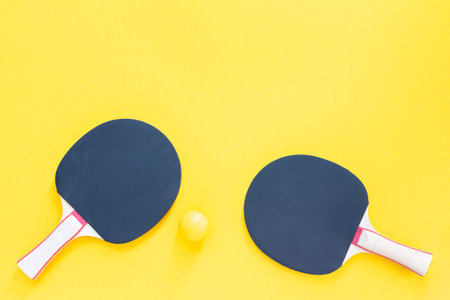 Black tennis rackets and orange balls isolated on a yellow background, sport equipment for table...