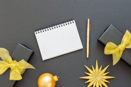 Holiday background, black background with glitter gold star and gift boxes , open spiral notepad and pen, flat lay, top view, copy spaceの写真素材