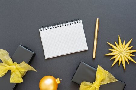 Holiday background, black background with glitter gold star and gift boxes , open spiral notepad and pen, flat lay, top view, copy spaceの写真素材