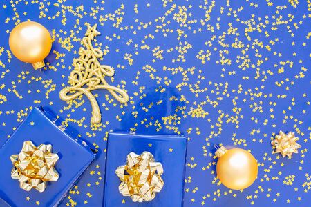 Gift boxes with a golden bow and fir tree with Christmas balls on  blueの写真素材