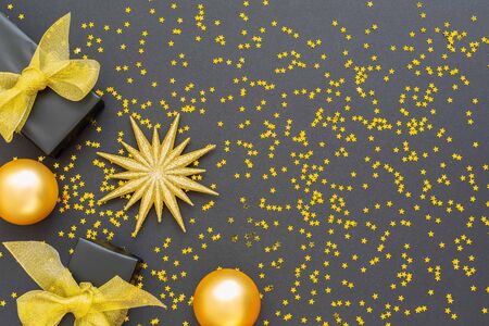 Festive background with gold decorations , shiny golden star and gift boxes and christmas balls on a black background with glitter gold stars , flat lay, top view, copy spaceの写真素材