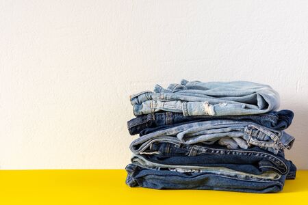 A stack of different jeans trousers close up on yellow and white background, casual clothesの写真素材