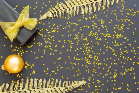 Festive background with gold decorations , shiny golden fern leaves and gift box with christmas balls on a black background with glitter gold stars , flat lay, top view, copy spaceの写真素材