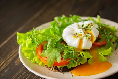 Light breakfast, poached egg with salad, tomatoes and arugula on dark breadの写真素材