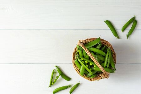 Fresh young green peas in a wicker basket, ripe organic vegetables, top viewの写真素材