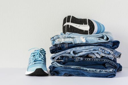 A stack of different jeans trousers and blue sneakers close up on white background, casual clothes , sports styleの写真素材