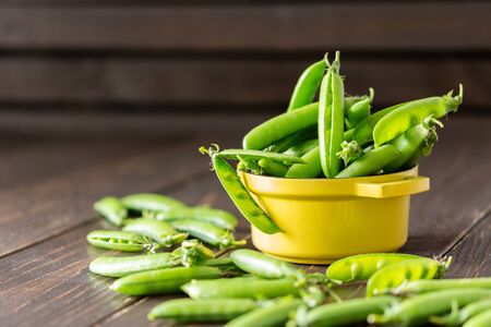 Fresh young green peas in pods in a yellow iron bowl, ripe organic vegetablesの写真素材