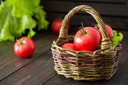 Fresh juicy ripe pink tomatoes with green ponytails in a wicker basket, a new crop of organic vegetablesの写真素材