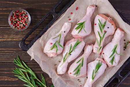Raw chicken drumsticks on a baking sheet on parchment with rosemary and spices on a wooden background, top viewの写真素材