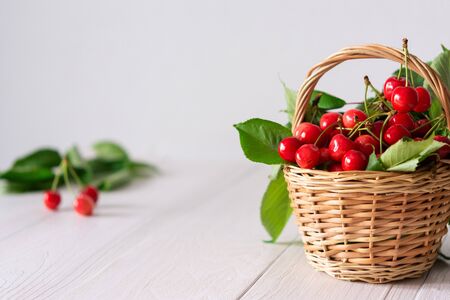 Ripe juicy cherries in a wicker basket on a white wooden backgroundの写真素材