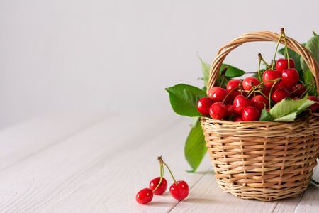 Ripe juicy cherries in a wicker basket on a white wooden backgroundの写真素材