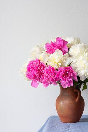 Beautiful bouquet of peonies in a clay pot stands on a table with a blue linen tableclothの写真素材