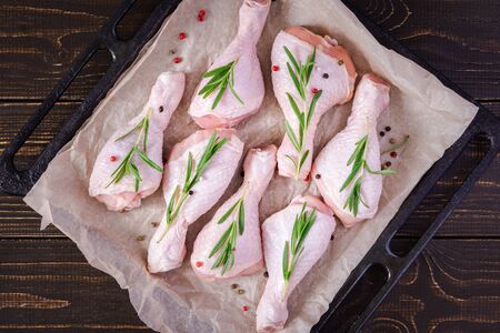 Raw chicken drumsticks on a baking sheet on parchment with rosemary and spices on a wooden background, top viewの写真素材