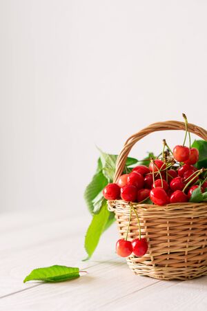 Ripe juicy cherries in a wicker basket on a white wooden backgroundの写真素材