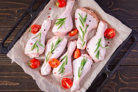 Raw chicken drumsticks on a baking sheet on parchment with rosemary and spices on wooden background , top viewの写真素材