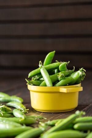Fresh young green peas in pods in a yellow iron bowl, ripe organic vegetablesの写真素材