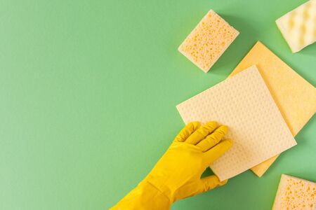 Hand in a yellow rubber glove with a cleaning sponges on a green backgroundの写真素材