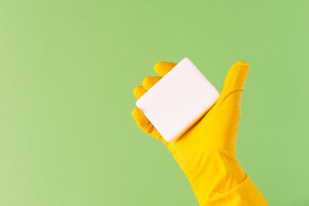 Hand in a yellow rubber glove with soap on a green backgroundの写真素材