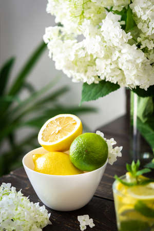 Vase of flowers viburnum opulus Roseum and plate with lemons and lime, refreshing lemonade with iceの写真素材