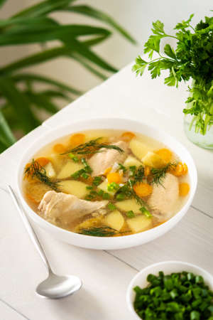 Chicken soup with fresh vegetables, chicken wings broth and young potatoes with onions and carrots, chopped green onions and parsleyの写真素材