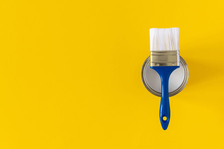 Can of white paint with a blue brush on a yellow background, painting, top view