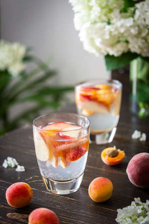 Refreshing drink with apricots and peaches, cold sparkling water with fruits, a vase of flowers viburnum opulus Roseum and a glass with a drinkの写真素材
